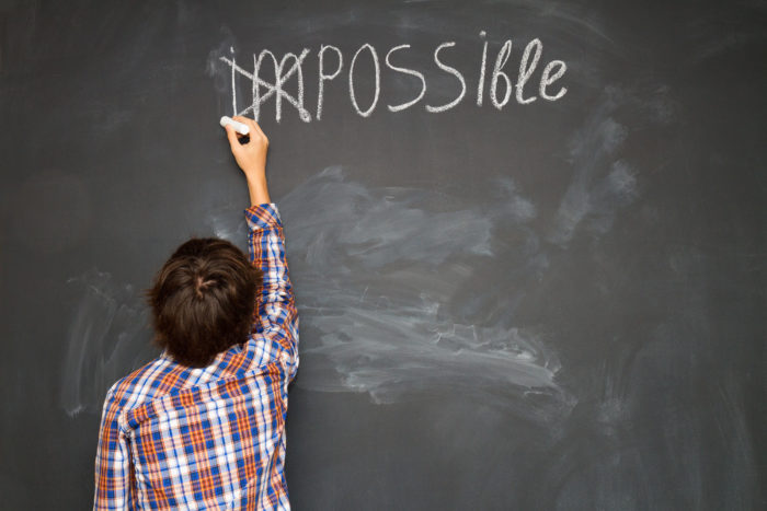 boy putting a cross over impossible on blackboard